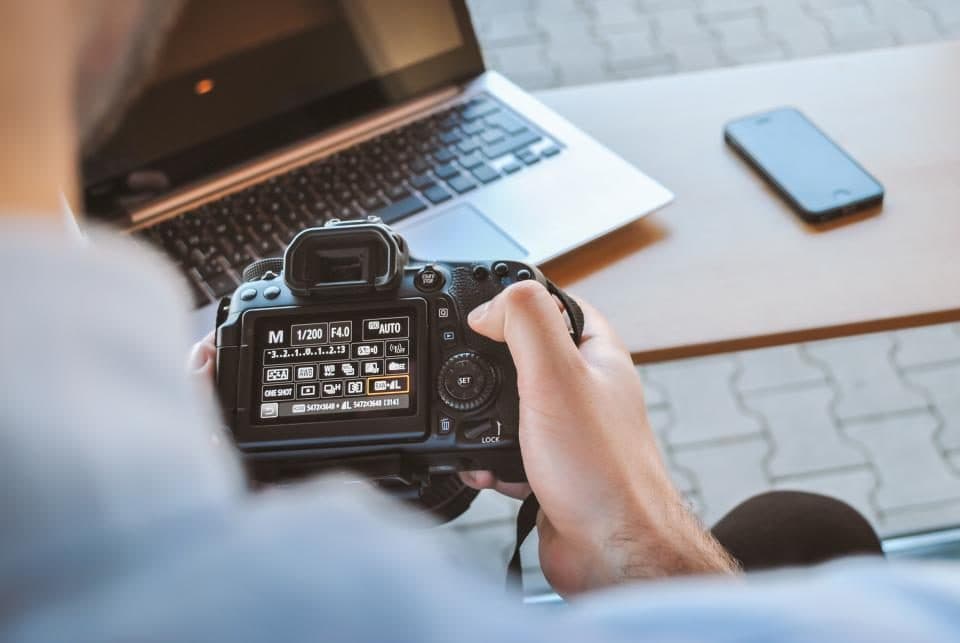 Person checking photos on a DSLR camera next to a laptop